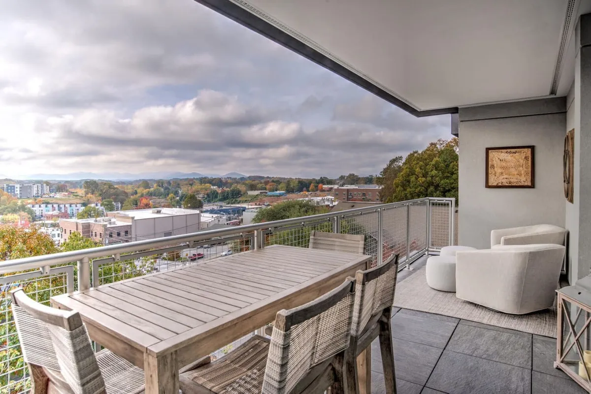 This exterior image highlights an outdoor dining table with comfortable chairs, scenic mountain views, and decorative wall art. The space is inviting for alfresco dining or relaxation, with a clear nod to both urban and natural elements.