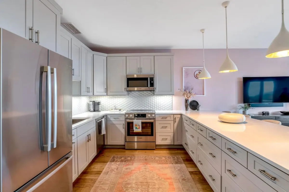 A beautifully lit kitchen featuring gleaming stainless steel appliances, a bright white quartz countertop, stylish pendant lighting, and a decorative rug. The space feels warm and welcoming, ideal for both casual breakfasts and festive gatherings.